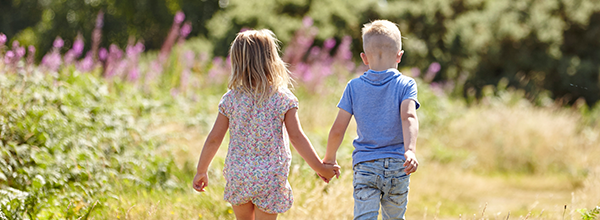 Two children holdings hands walking through a meadow
